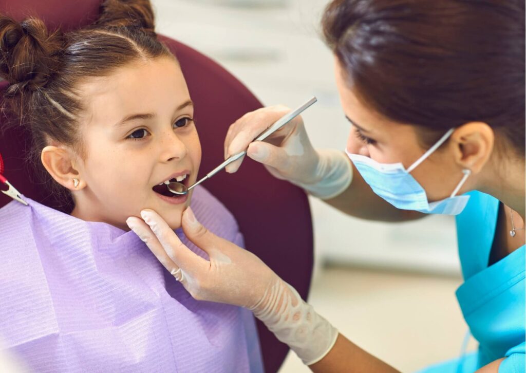 Pediatric dentist examining a child's teeth during a checkup to monitor when kids lose their first tooth.